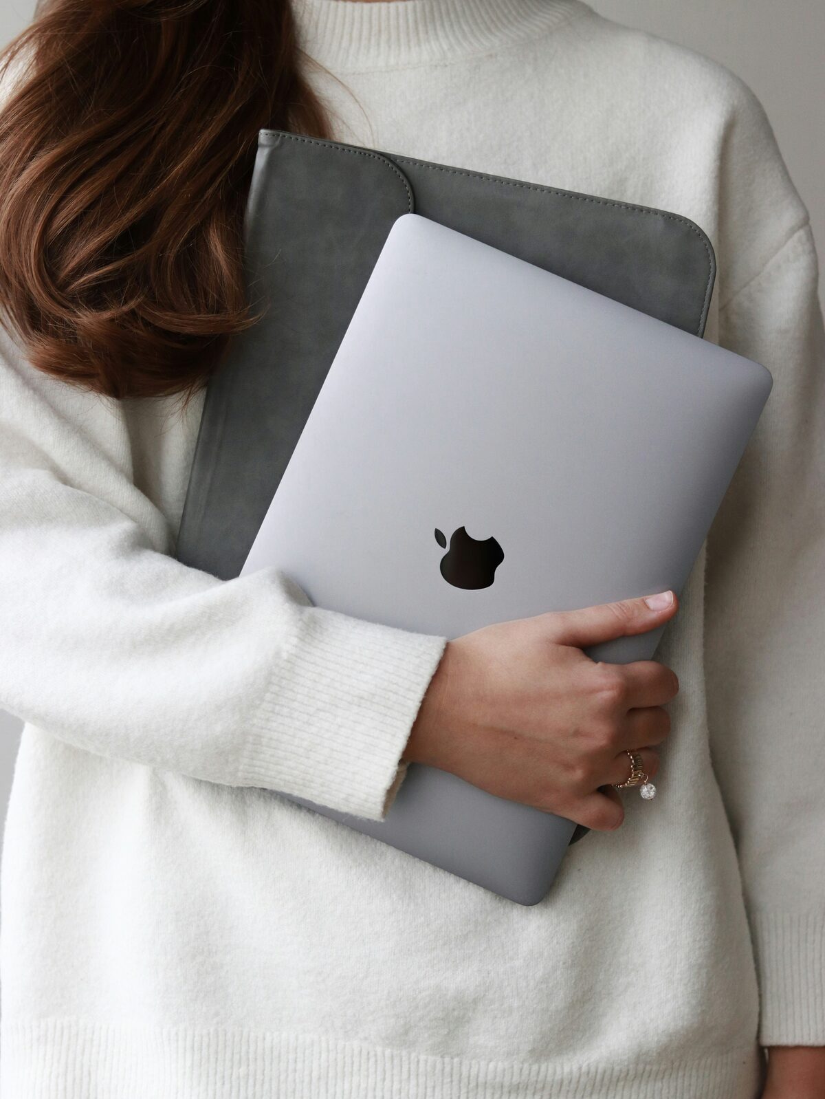 Empreendedora de suéter branco segurando um notebook junto ao corpo
